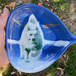 May include: A blue and white ceramic dish with a white silhouette of a dog on a blue background. The dish has a gold design and the signature "Matt St. John" is visible in the lower right corner.