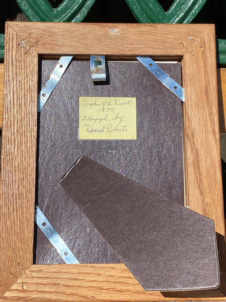 May include: A wooden picture frame with a brown mat and a yellow note attached to the mat. The note reads "Arab of the Desert 1839 Lithograph by David Roberts".