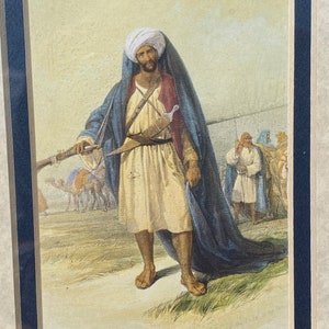 May include: A watercolor painting of a man in traditional Middle Eastern clothing, holding a rifle and standing in a desert landscape. He is wearing a white turban, a blue robe, and a white sash. There are camels and other figures in the background.
