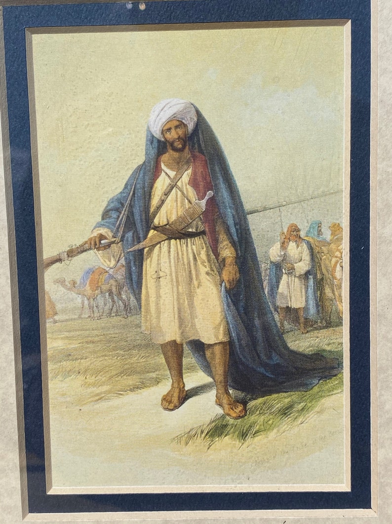 May include: A watercolor painting of a man in traditional Middle Eastern clothing, holding a rifle and standing in a desert landscape. He is wearing a white turban, a blue robe, and a white sash. There are camels and other figures in the background.