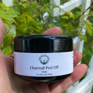 May include: A black jar with a white label that reads "Hippie Pharm Charcoal Peel Off Mask 2.1 OZ/62.10 ML".