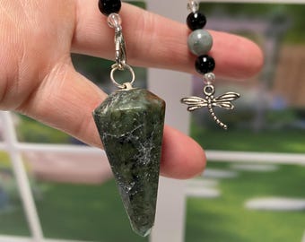 May include: A green crystal pendulum with a silver chain and dragonfly charm. The chain has black and grey beads.