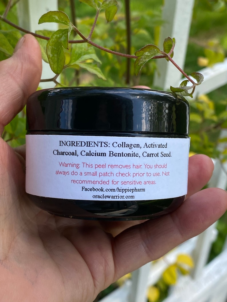 May include: A black jar with a white label that reads "INGREDIENTS: Collagen, Activated Charcoal, Calcium Bentonite, Carrot Seed. Warning: This peel removes hair. You should always do a small patch check prior to use. Not recommended for sensitive areas. Facebook.com/hippiepharm oraclewarrior.com"