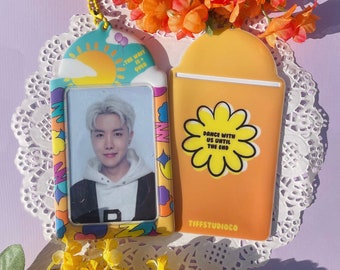 May include: A colorful plastic ID card holder with a photo of a person with blonde hair. The holder has a yellow sun and clouds on the top and the text "The wait is over". The back of the holder is orange with a yellow flower and the text "Dance with us until the end". The holder has the text "Tiffstudioco" at the bottom.