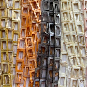 May include: Rows of square shell belt buckles in various colors. The colors include yellow, orange, gray, white, and pink. The buckles are made of a natural material and have a glossy finish. The buckles are arranged in vertical rows.