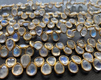 May include: A strand of iridescent white moonstone beads with gold-toned accents. The beads are teardrop shaped and have a smooth, polished finish.