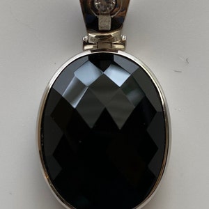 May include: A silver pendant with a black oval gemstone and a small clear rhinestone.