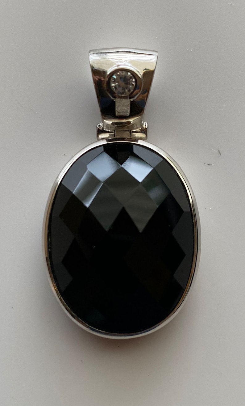 May include: A silver pendant with a black oval gemstone and a small clear rhinestone.