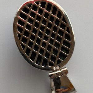 May include: Silver oval pendant with a black grid pattern and a silver bail. The pendant is marked "925" on the back.