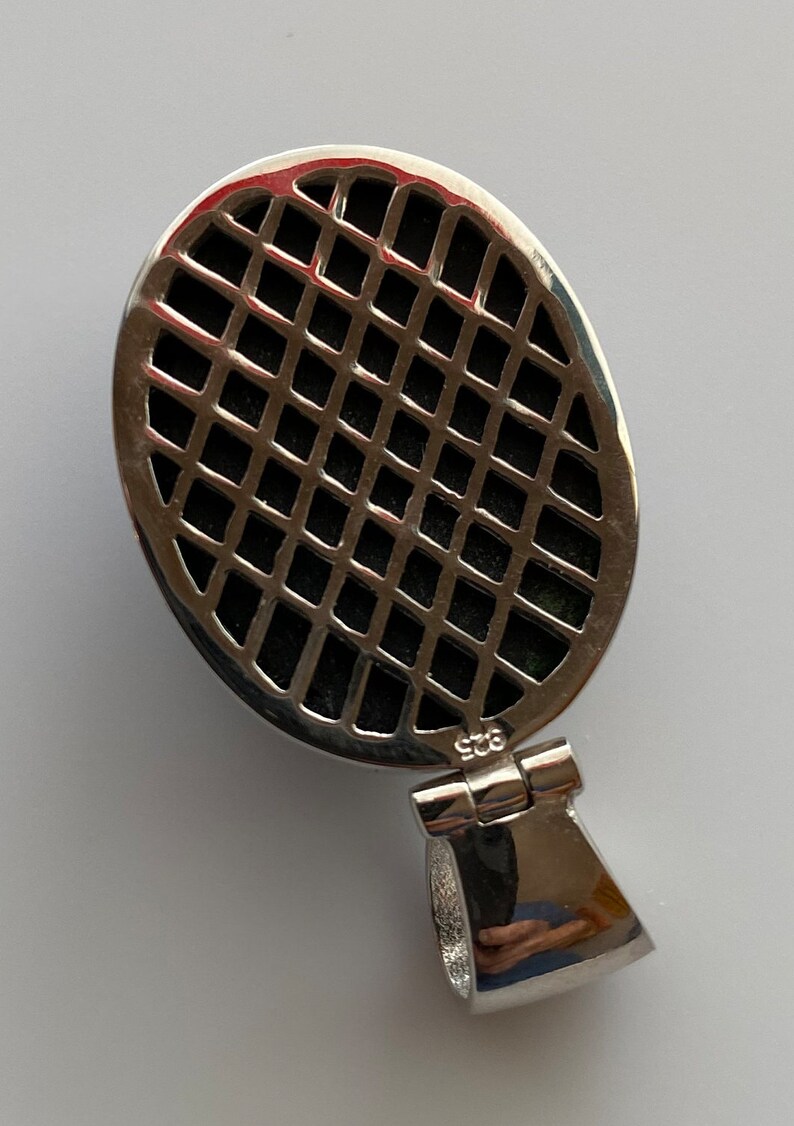 May include: Silver oval pendant with a black grid pattern and a silver bail. The pendant is marked "925" on the back.