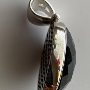May include: A silver pendant with a black faceted gemstone. The pendant has a detailed design on the side.