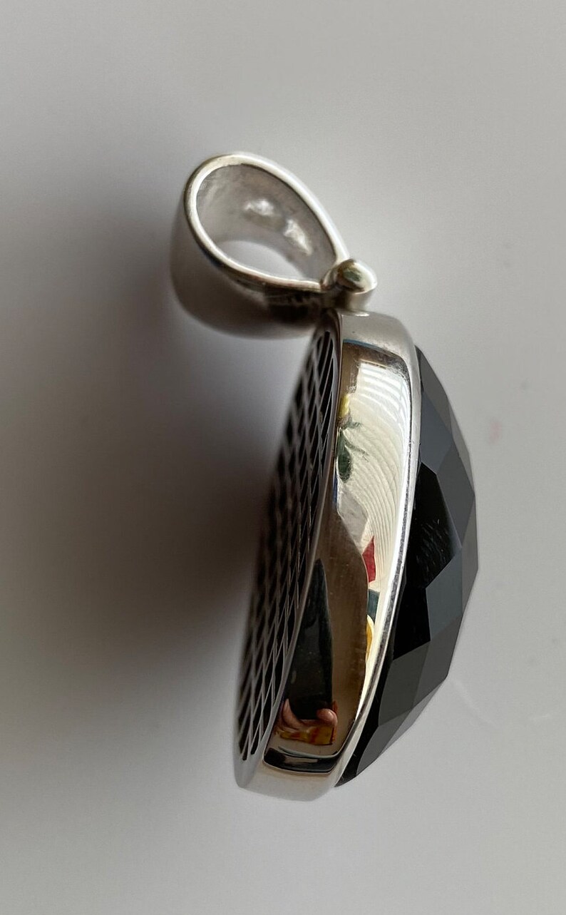 May include: A silver pendant with a black faceted gemstone. The pendant has a detailed design on the side.