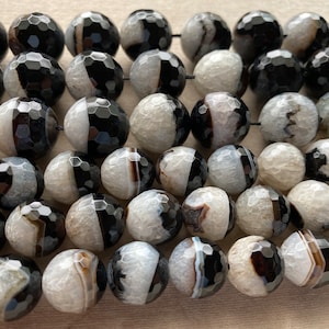 May include: A strand of black and white agate beads with a faceted, rounded shape. The beads have a natural, organic look and are perfect for jewelry making.