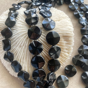 May include: Two strands of black gemstone beads. The beads are faceted and have a starburst design. The beads are strung on a white cord.