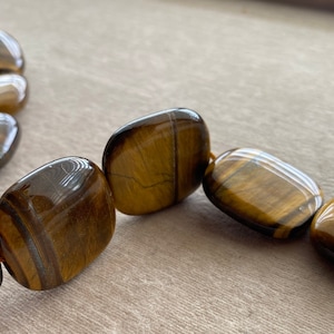 May include: A strand of tiger's eye beads, each bead is a smooth, polished, rectangular shape with a golden brown color and a distinctive chatoyancy effect.
