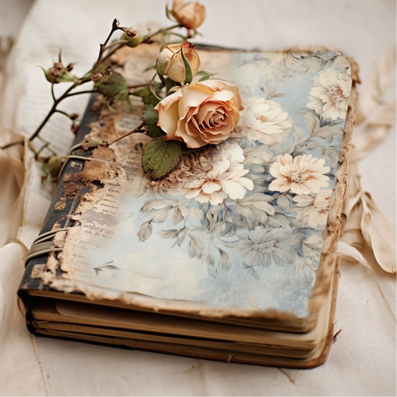 May include: A vintage, worn journal with a floral design on the cover. The journal is closed and has a faded blue and white floral pattern. A single rose and a few buds are resting on the cover.