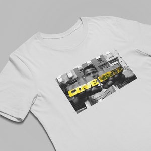 May include: A white t-shirt with a black and white photo of a person holding gold letters that spell "LOVE HATE".