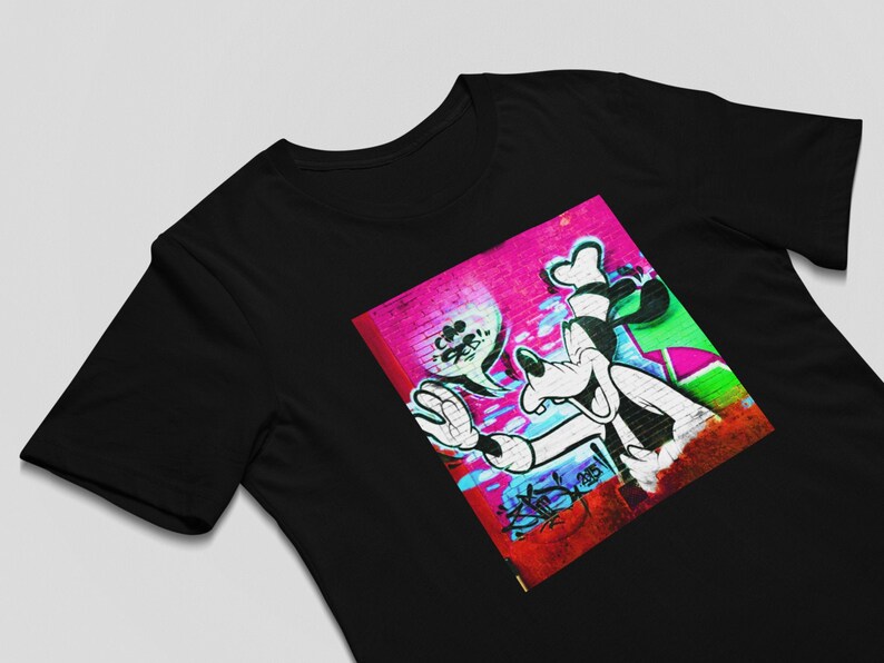May include: Black t-shirt with a colorful graphic print of a cartoon dog on a pink and green brick wall. The dog is wearing a white hat and has a big smile.