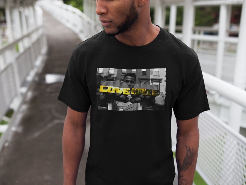 May include: Black t-shirt with a black and white photo of a person holding gold letters that spell "LOVE HATE".
