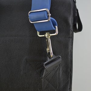 Puede incluir: Un bolso de cuero negro con una correa ajustable azul y un cierre de gancho plateado.