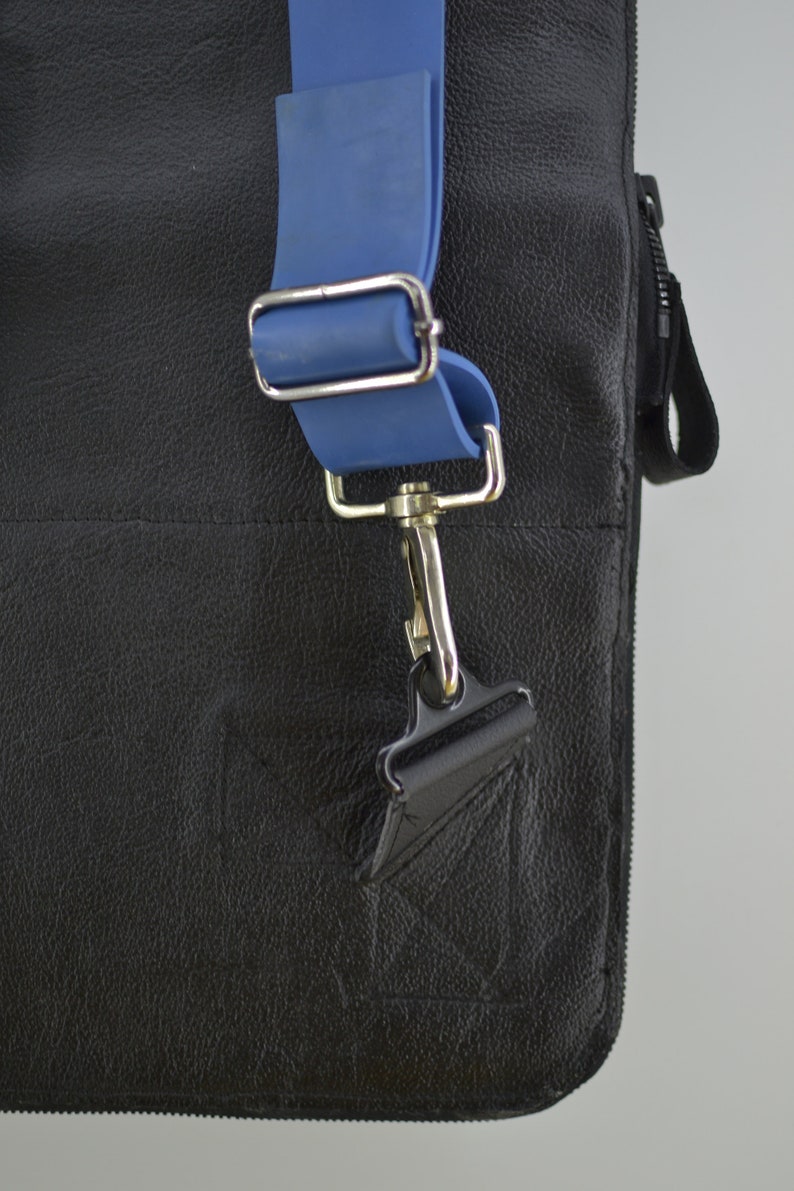 Puede incluir: Un bolso de cuero negro con una correa ajustable azul y un cierre de gancho plateado.