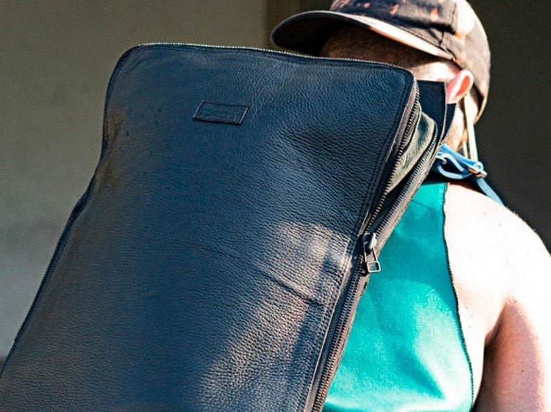 Puede incluir: Una mochila de cuero negro con cierre de cremallera. La mochila la lleva puesta una persona que lleva un top de tirantes turquesa.