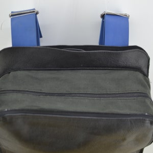 Puede incluir: Una bolsa de lona negra con dos correas azules y un cierre de cremallera.