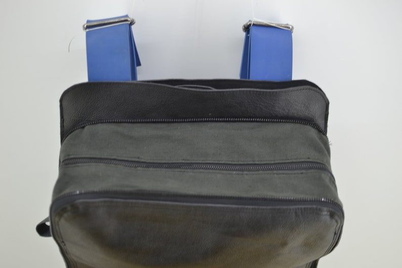 Puede incluir: Una bolsa de lona negra con dos correas azules y un cierre de cremallera.