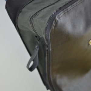 Puede incluir: Primer plano de una bolsa de cuero negro con cremallera y un tirador de cremallera negro. La bolsa tiene una superficie lisa y texturizada.