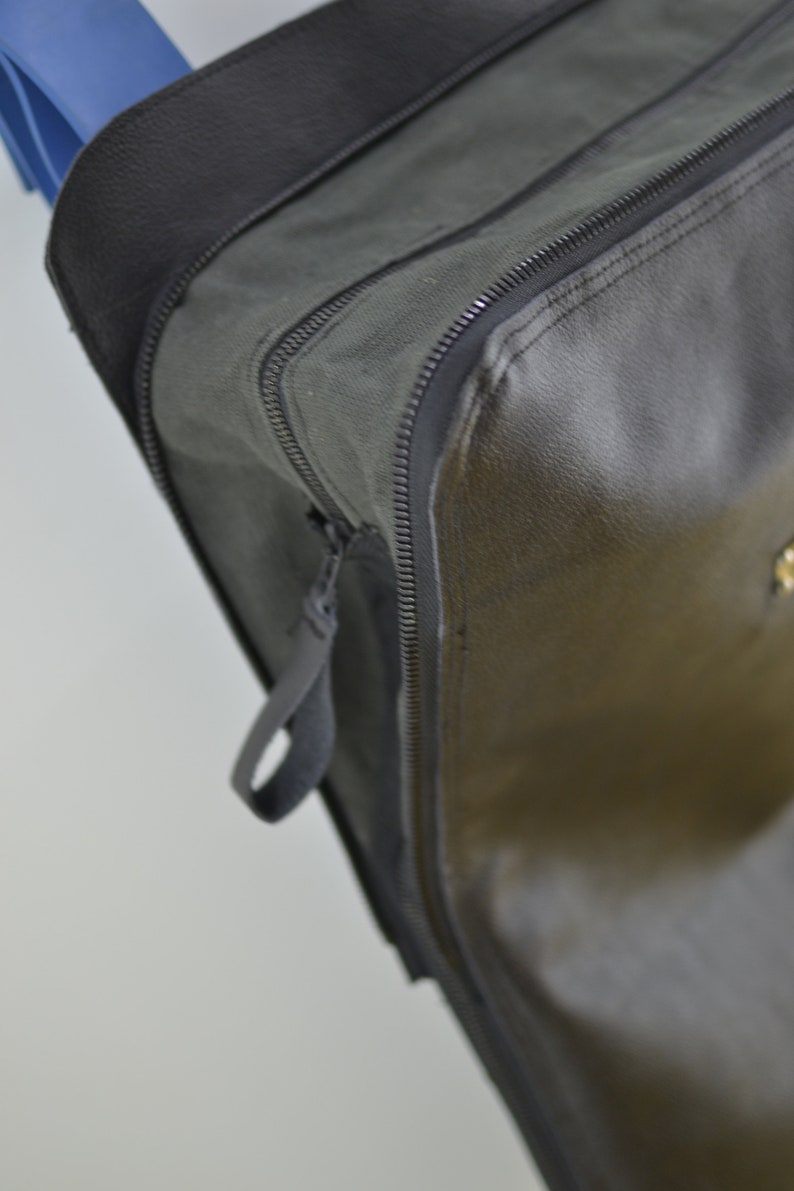 Puede incluir: Primer plano de una bolsa de cuero negro con cremallera y un tirador de cremallera negro. La bolsa tiene una superficie lisa y texturizada.