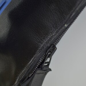 Puede incluir: Primer plano de una cremallera de cuero negro con una leng&uuml;eta azul. La cremallera est&aacute; en una bolsa de cuero negro.