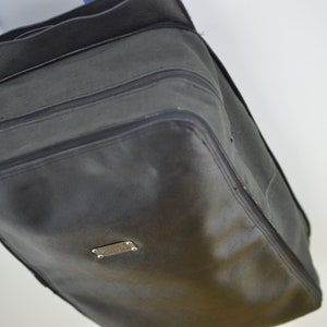 Puede incluir: Una bolsa de viaje de lona verde oscuro con una cremallera negra y una etiqueta de metal plateado. La bolsa tiene una forma rectangular y est&aacute; hecha de un material duradero.
