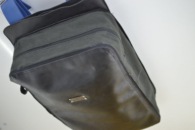 Puede incluir: Una bolsa de viaje de lona verde oscuro con una cremallera negra y una etiqueta de metal plateado. La bolsa tiene una forma rectangular y est&aacute; hecha de un material duradero.