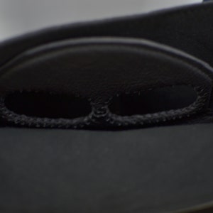 Puede incluir: Primer plano del interior de un bolso de cuero negro con dos peque&ntilde;os recortes redondos para las asas.