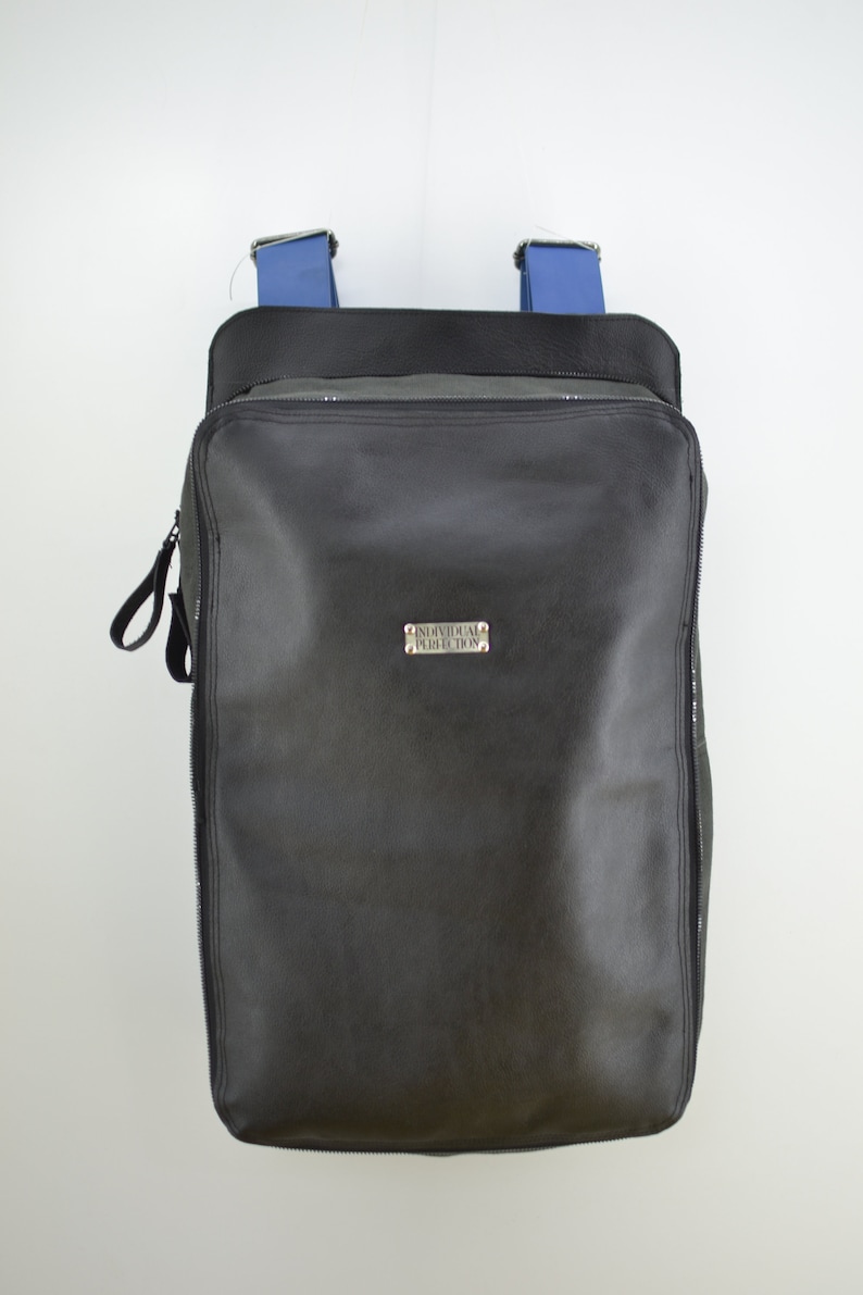Puede incluir: Mochila de cuero negro con correas azules y una etiqueta de metal plateado que dice "Individual Perfection".