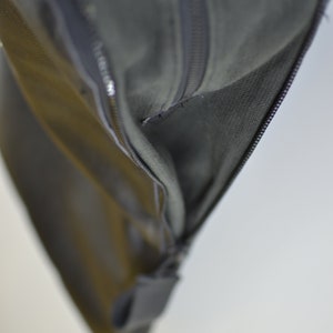 Puede incluir: Primer plano de una bolsa de cuero negro con cremallera y forro gris. La bolsa est&aacute; parcialmente abierta, revelando el forro.