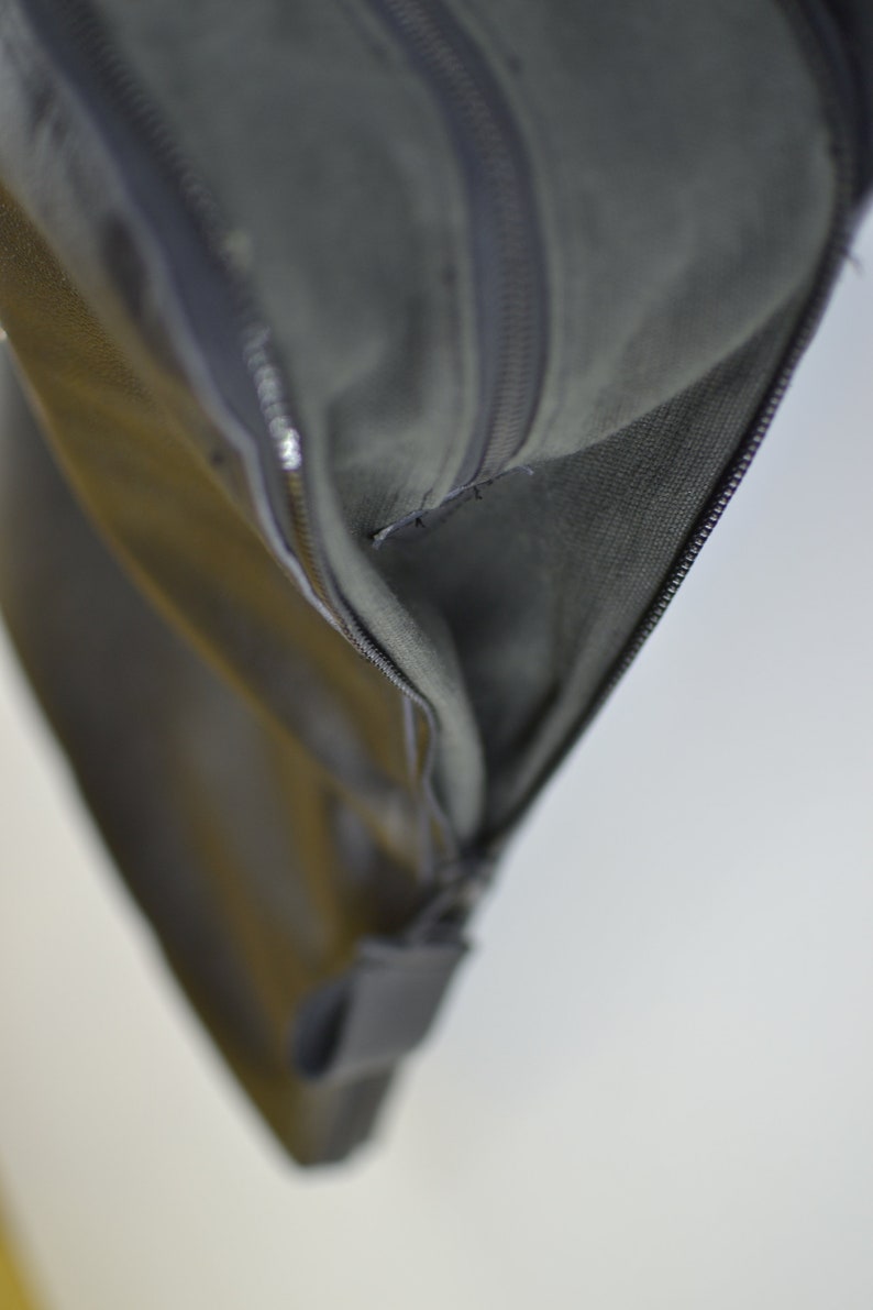Puede incluir: Primer plano de una bolsa de cuero negro con cremallera y forro gris. La bolsa est&aacute; parcialmente abierta, revelando el forro.