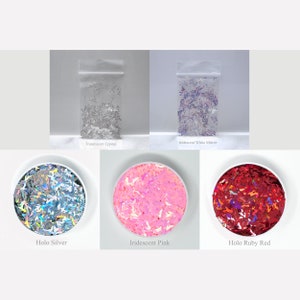 May include: Assortment of iridescent glitter in various colors, including silver, pink, and red. The glitter is packaged in small plastic bags and displayed in clear bowls.