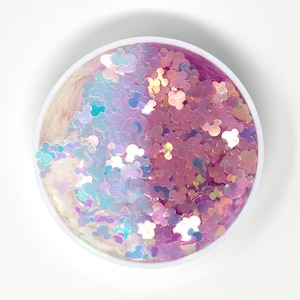 May include: A close-up of a round container filled with iridescent pink and white glitter shaped like Mickey Mouse heads.