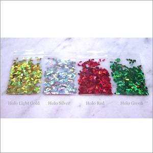 May include: Four small bags of holographic glitter in the colors light gold, silver, red, and green. Each bag contains pineapple-shaped glitter.