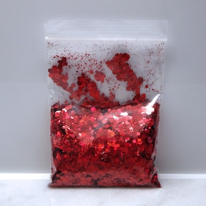 May include: A clear plastic bag filled with red glitter. The glitter is in various sizes and shapes, with a holographic finish.