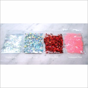 May include: Four small bags of iridescent glitter in the colors crystal blue, holo silver, ruby red, and iridescent pink. The glitter is shaped like small, flat butterflies.