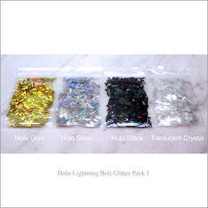 May include: Four small bags of holographic glitter in gold, silver, black, and clear. The bags are labeled "Holo Gold", "Holo Silver", "Holo Black", and "Translucent Crystal". The text "Holo Lightning Bolt Glitter Pack I" is below the bags.