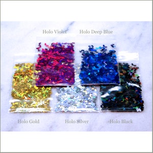 May include: Six small bags of holographic glitter in the shapes of music notes. The bags are labeled "Holo Gold", "Holo Silver", "Holo Black", "Holo Violet", "Holo Deep Blue".