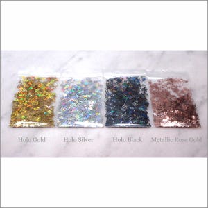 May include: Four small bags of holographic letter confetti. The bags are labeled "Holo Gold", "Holo Silver", "Holo Black", and "Metallic Rose Gold".