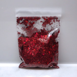 May include: A clear plastic bag filled with red glitter. The glitter is a mix of small and large pieces, creating a sparkly effect.