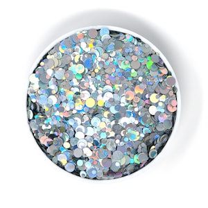 May include: A white bowl filled with iridescent silver glitter confetti. The confetti is a mix of different sizes and shapes.