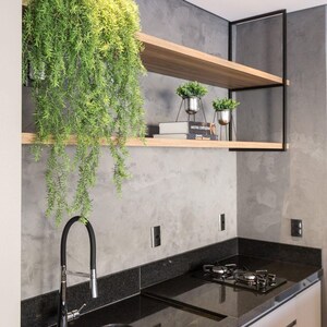 May include: Contemporary kitchen with a black granite worktop, stainless steel sink, and gas hob. Wooden shelving displays potted plants and books. A trailing green plant hangs down, adding a natural element to the design.