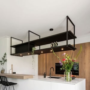May include: A modern kitchen with white cabinets and a large island. The island has a black worktop and a black tap. There are black metal shelves above the island, and a vase of flowers on the worktop.