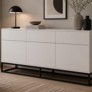 Peut inclure: Un buffet rectangulaire blanc doté de trois portes de placard et de trois tiroirs, reposant sur une base en cadre métallique noir. Le meuble présente un design épuré à façade plate avec des lignes horizontales séparant les tiroirs des portes.